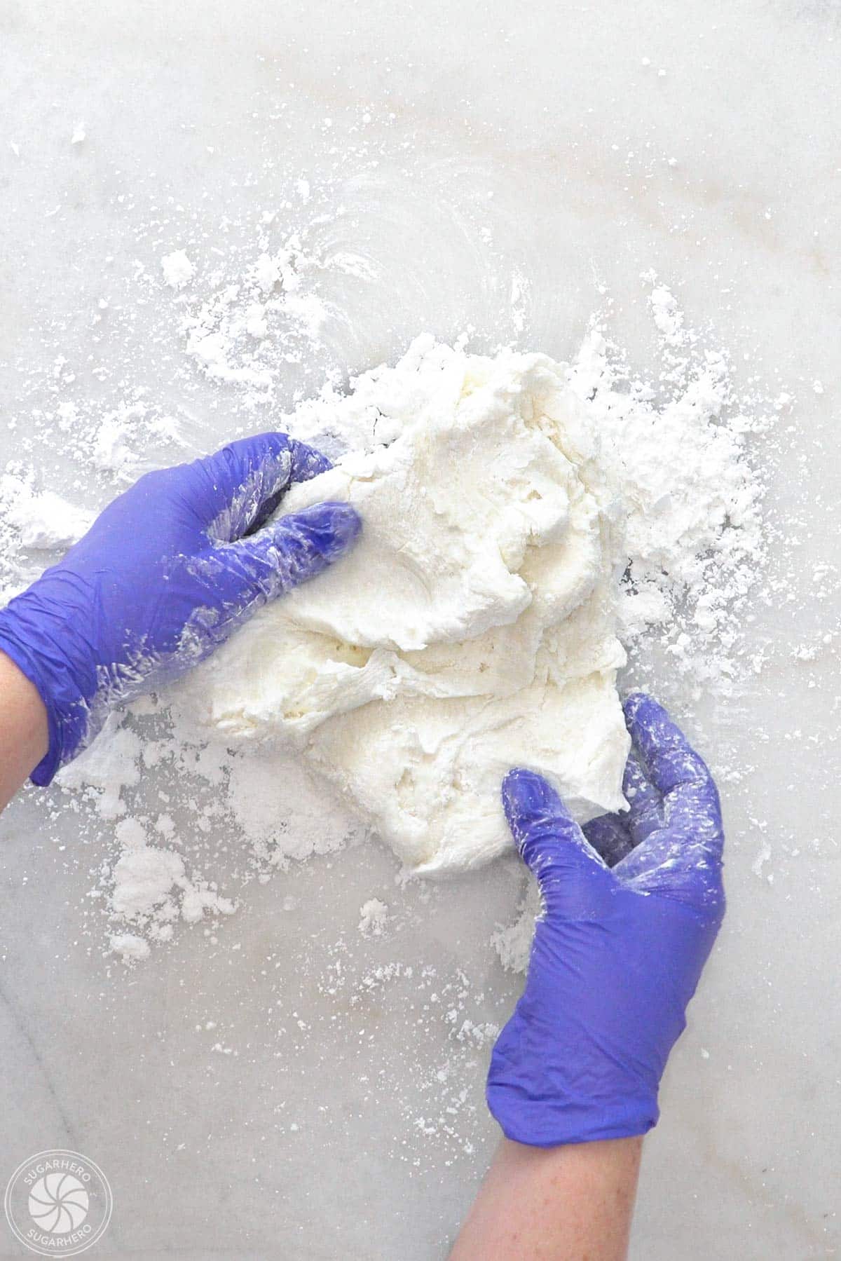 Gloved hands mixing more powdered sugar into white fondant.
