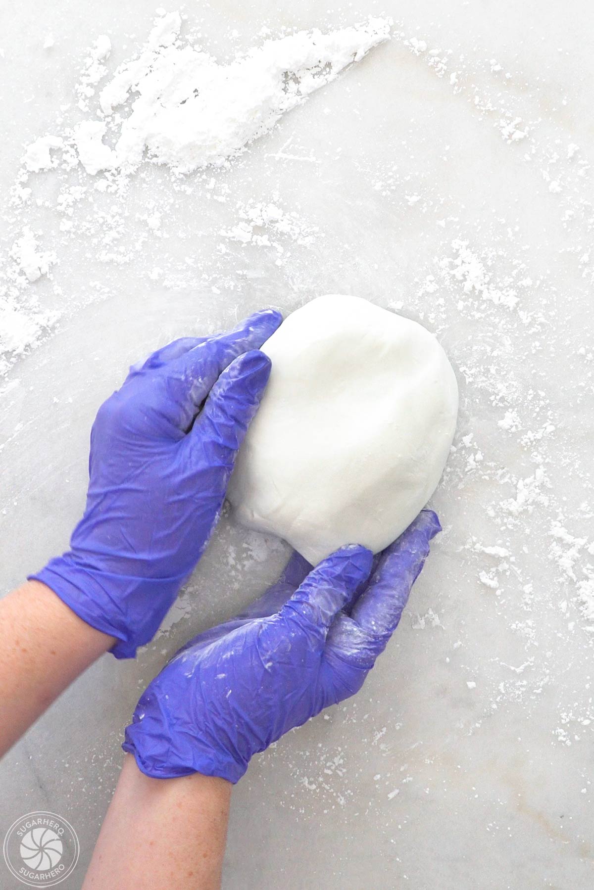 Gloved hands holding a ball of freshly made white fondant.