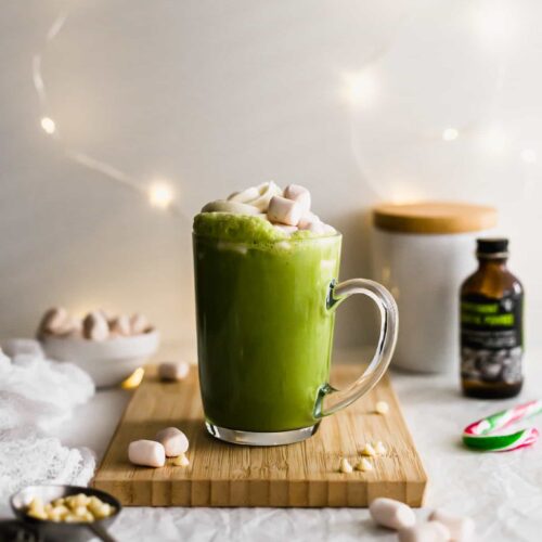 Cup of Matcha Peppermint White Hot Chocolate on a wooden cutting board with white lights in the background.