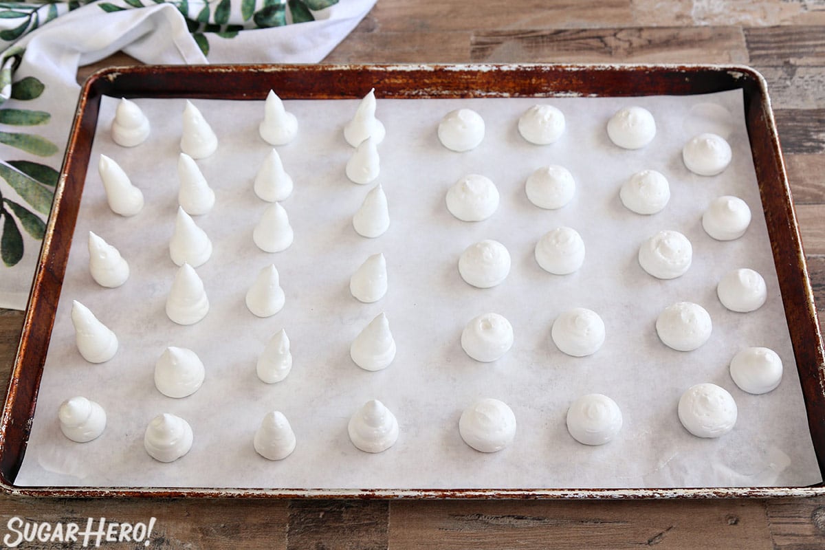 Baking sheet with meringues piped in the shape of mushroom stems and caps for Meringue Mushrooms.