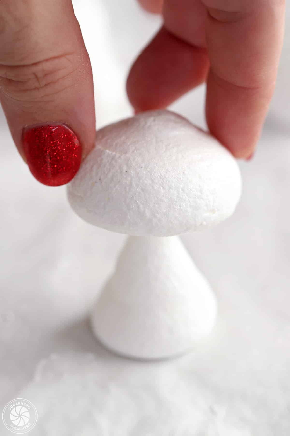 Placing a meringue mushroom cap on a mushroom stem.
