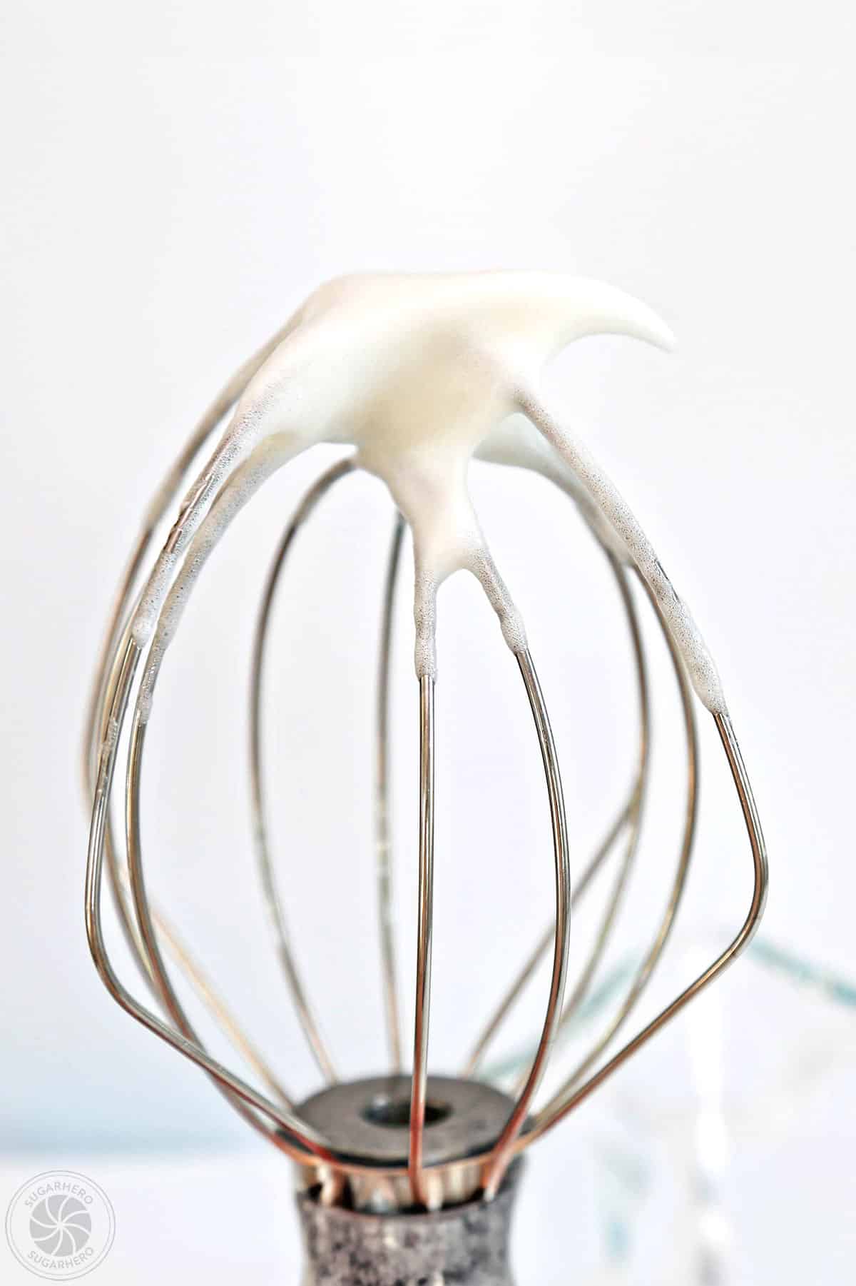 A whisk displaying egg whites whipped to soft peaks.