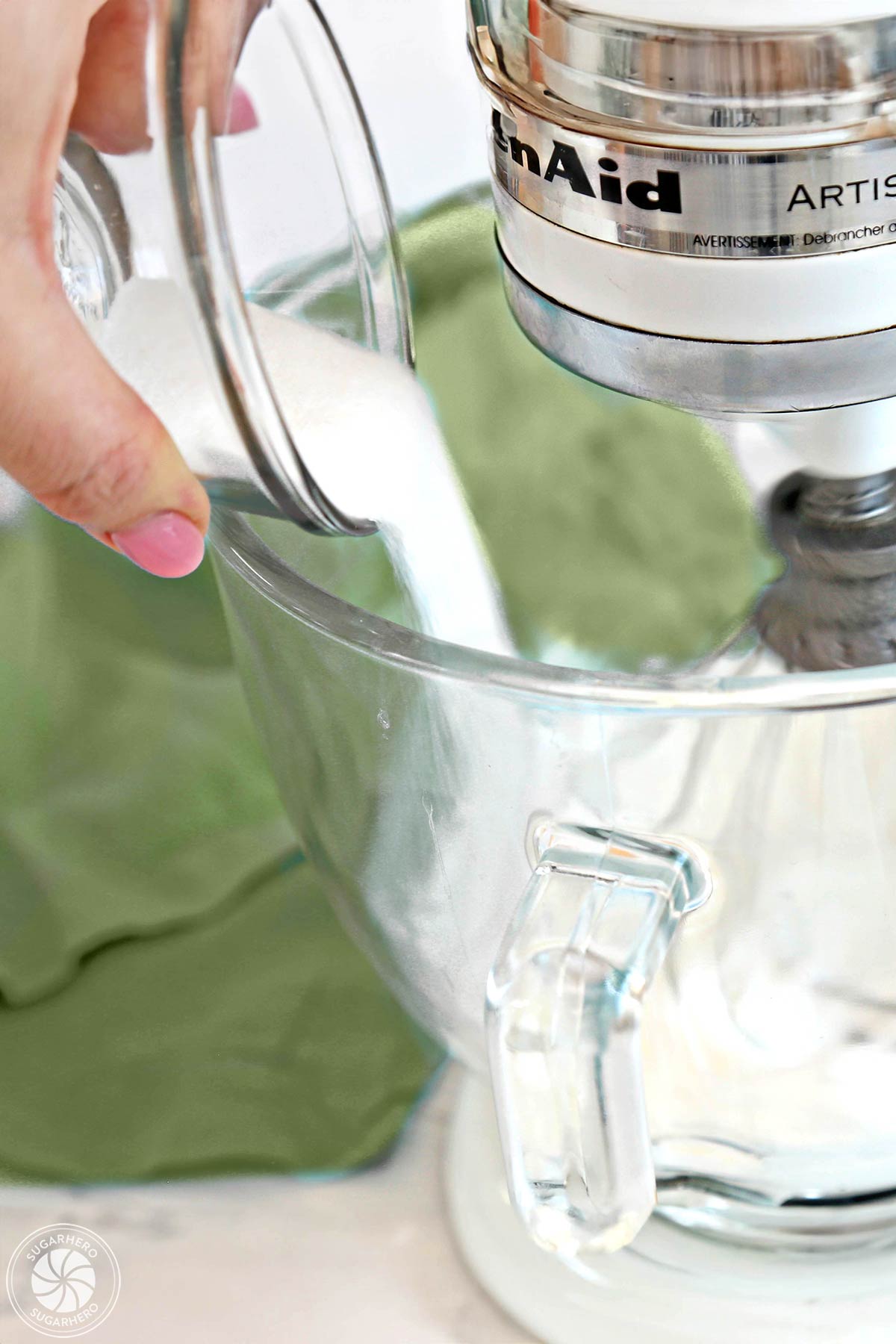 Pouring granulated sugar into a mixing bowl with whipped egg whites.