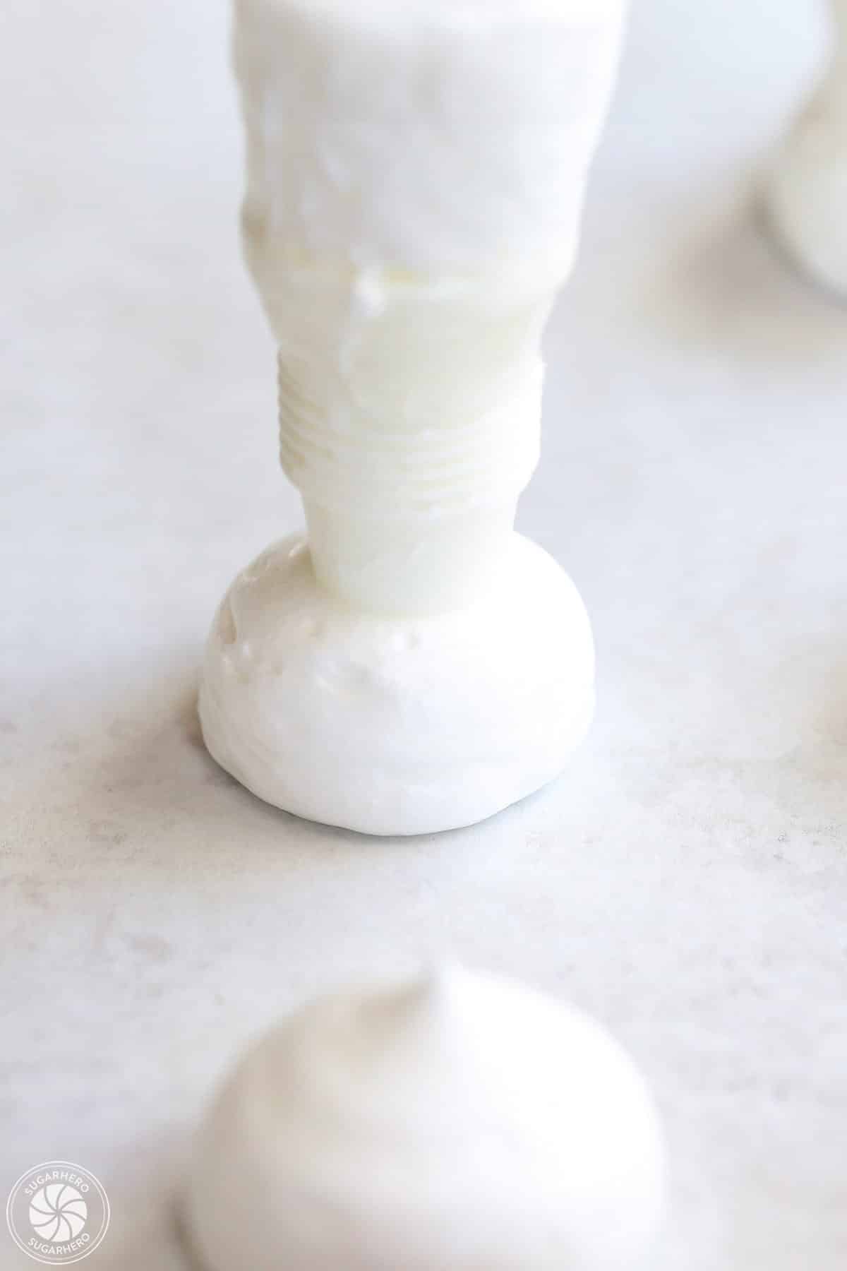 Piping a round meringue mushroom cap on parchment paper.
