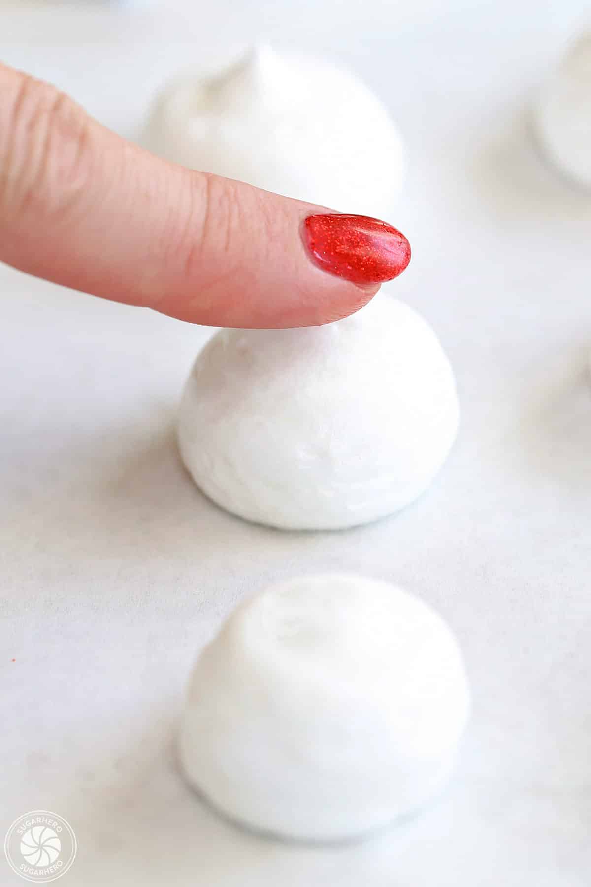 Flattening the top of a meringue mushroom cap with a fingertip.