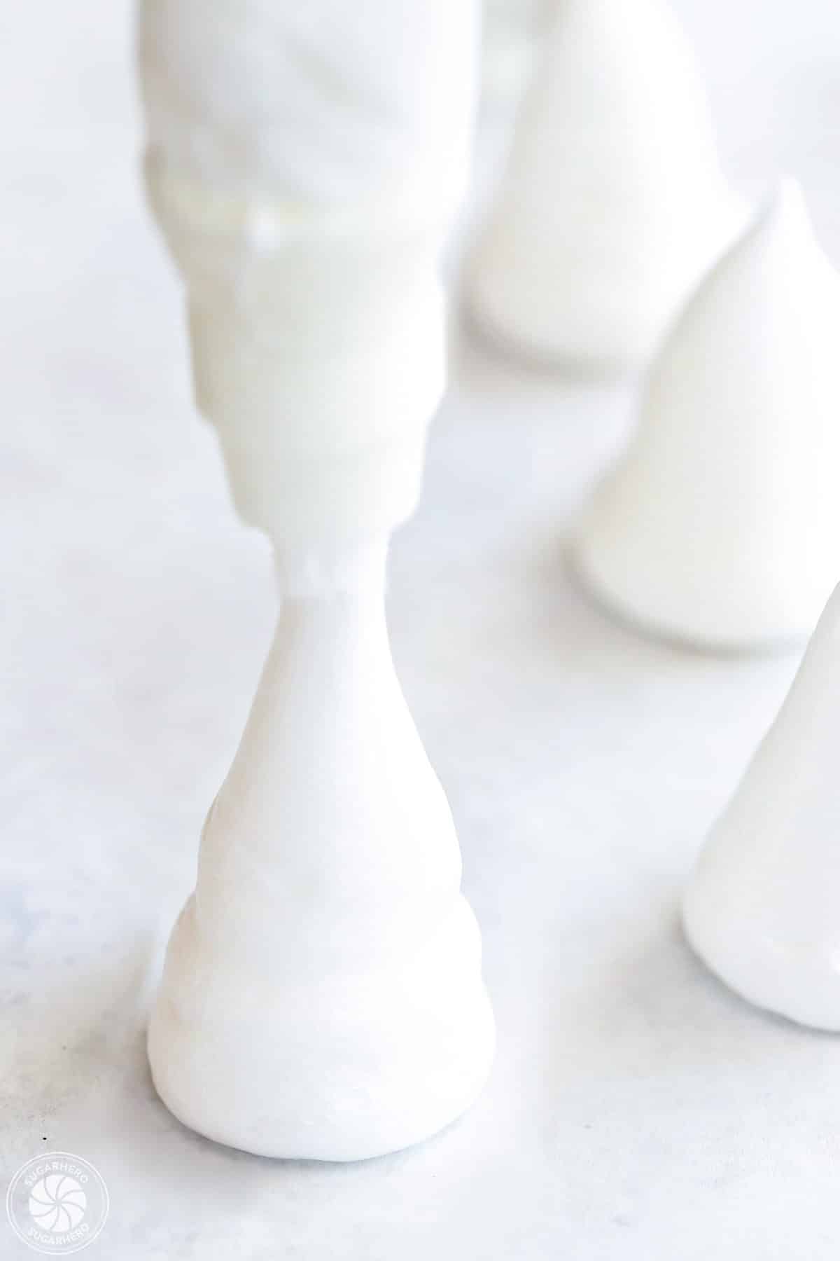 Piping a meringue mushroom stem on a piece of parchment paper.