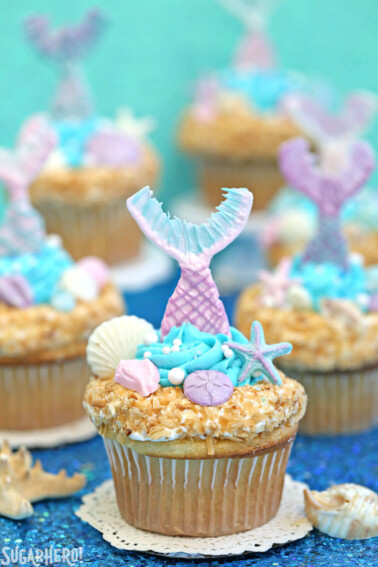 Several Mermaid Cupcakes on a blue shiny surface.