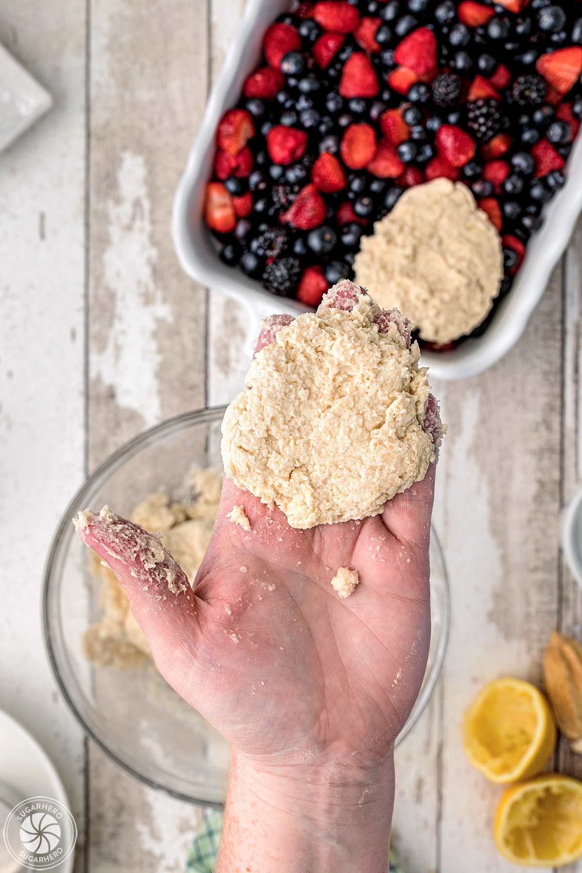 Hand showing how to flatten the dough for the crust before placing it on top of the berry cobbler.