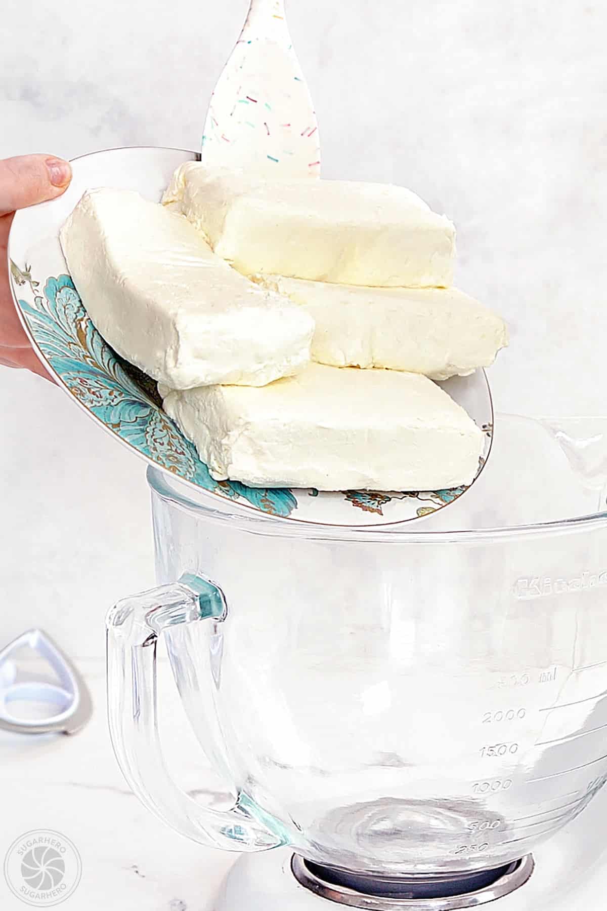 Hand pushing cream cheese into a mixing bowl.