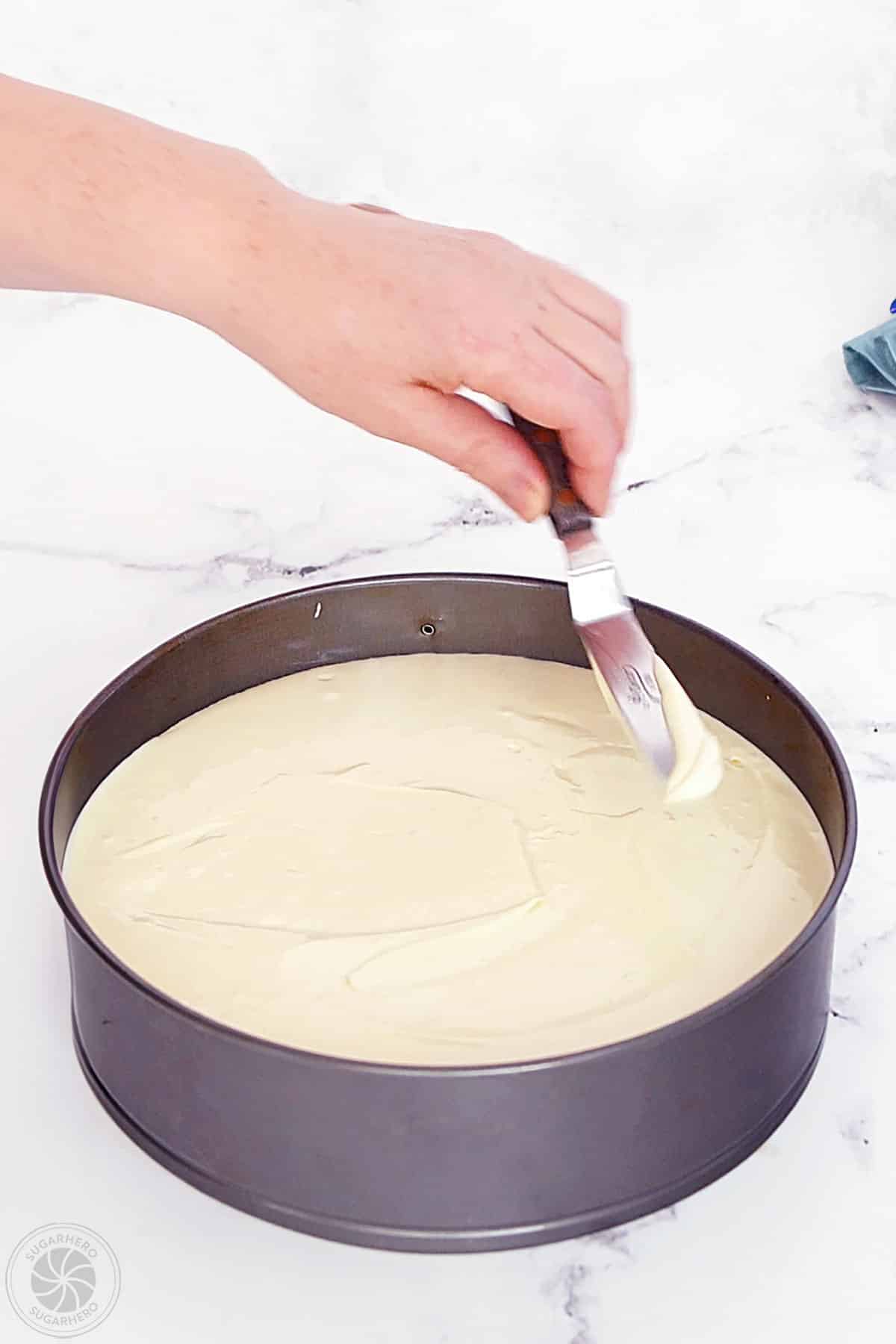 Hand using a spatula to spread out the top of the cheesecake batter.
