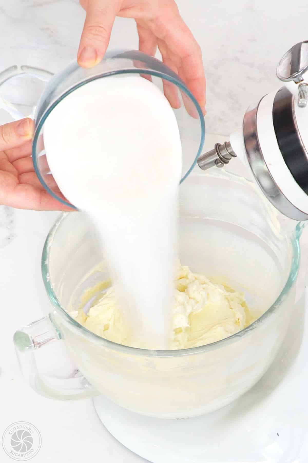 Hand pouring sugar into whipped cream cheese.