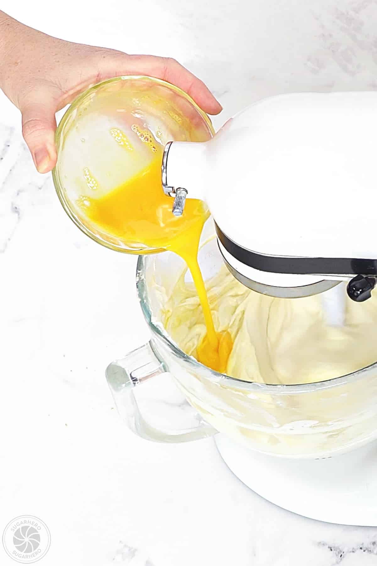 Pouring whisked eggs into cheesecake batter in a mixing bowl.