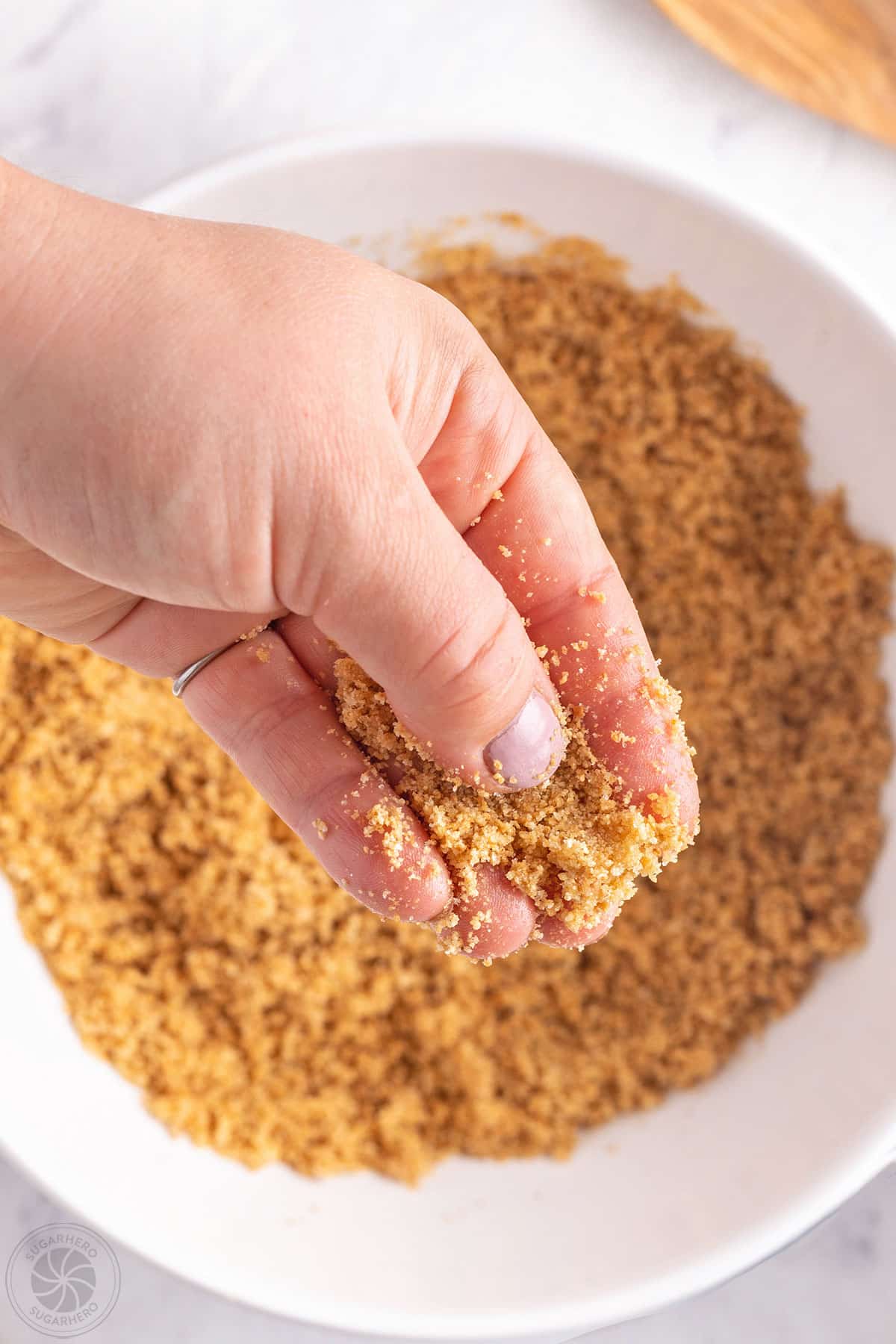 Hand holding graham cracker crust mixture over a bowl.
