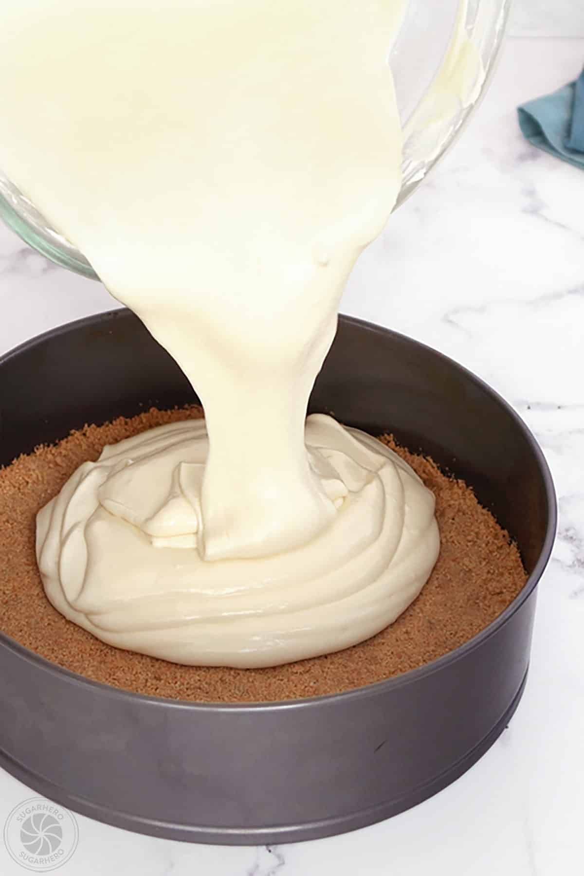 Pouring cheesecake batter over graham cracker crust in a springform pan.