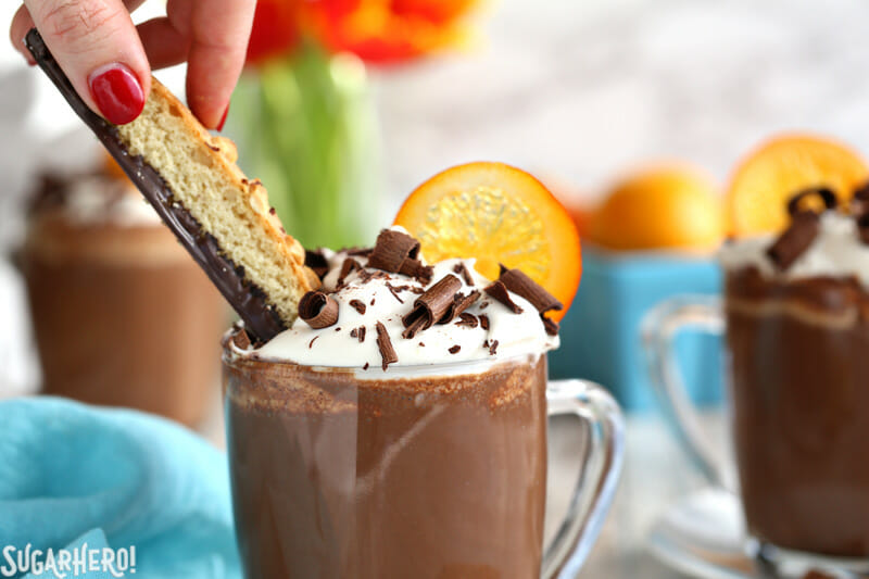 Hand dipping chocolate biscotti into a mug of Orange Hot Chocolate | From SugarHero.com