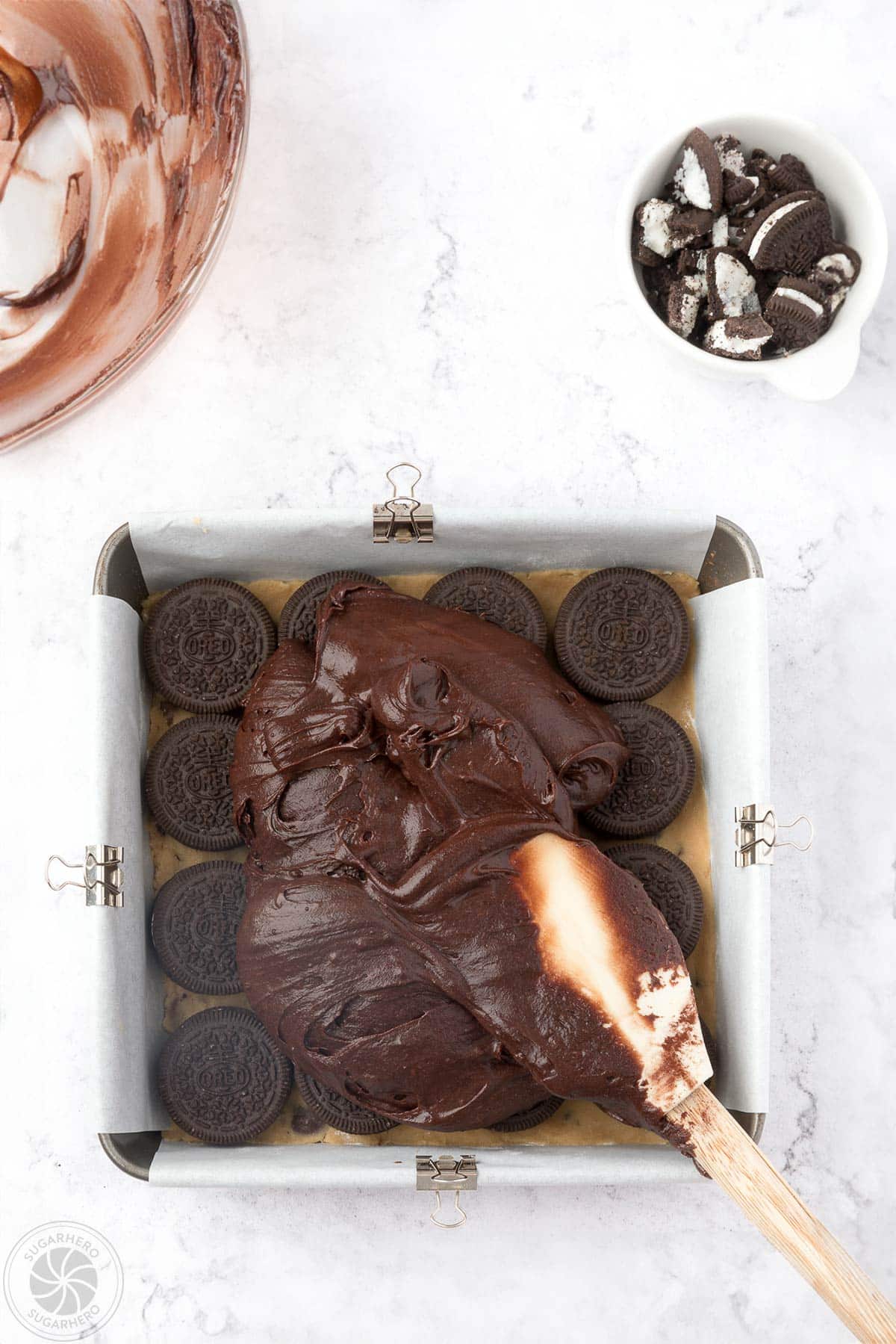 Spreading brownie batter on chocolate chip cookie dough and Oreos in a square pan.