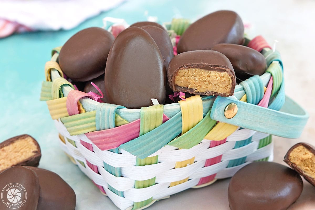 Peanut butter eggs in and around a colorful Easter basket with some eggs cut in half to show the filling.