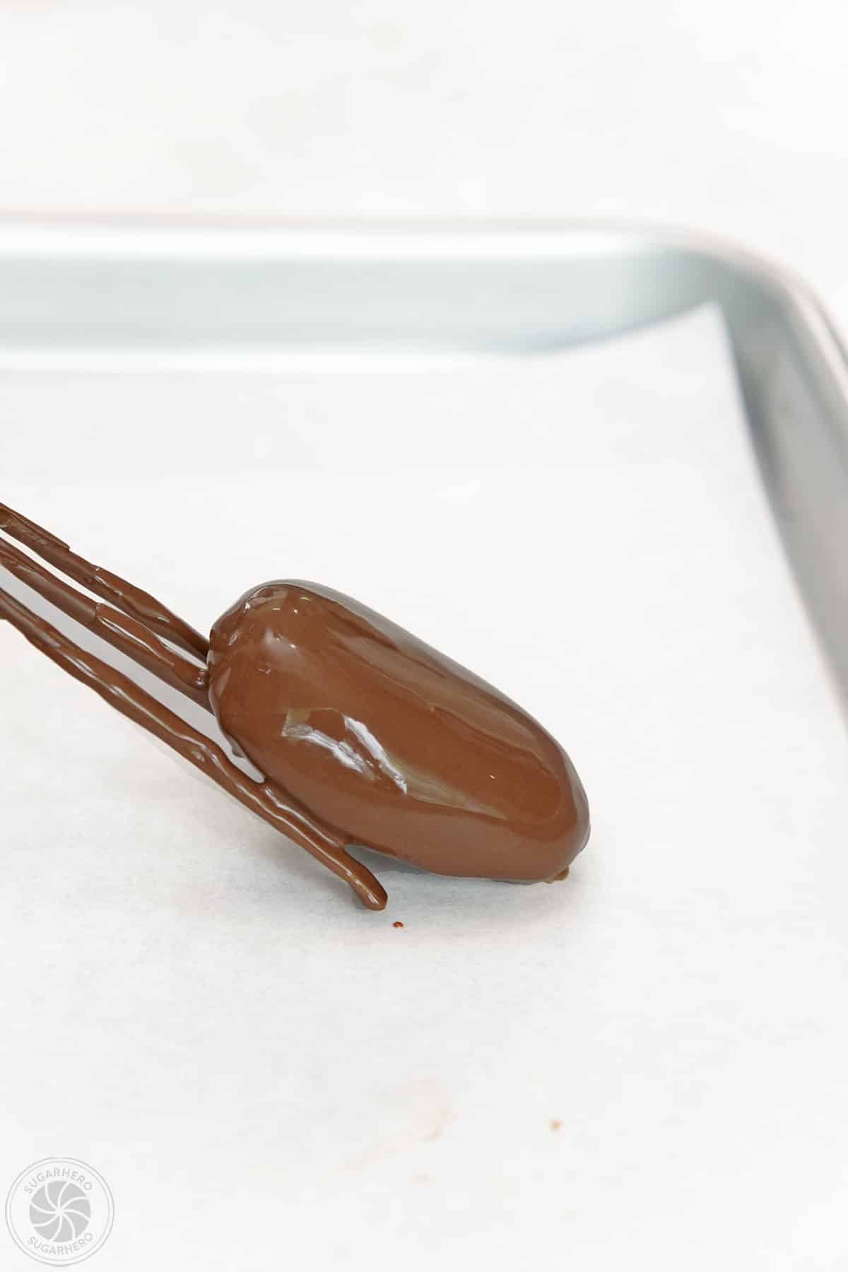 A dipping fork gently laying down a dipped peanut butter egg on a parchment-lined baking sheet.