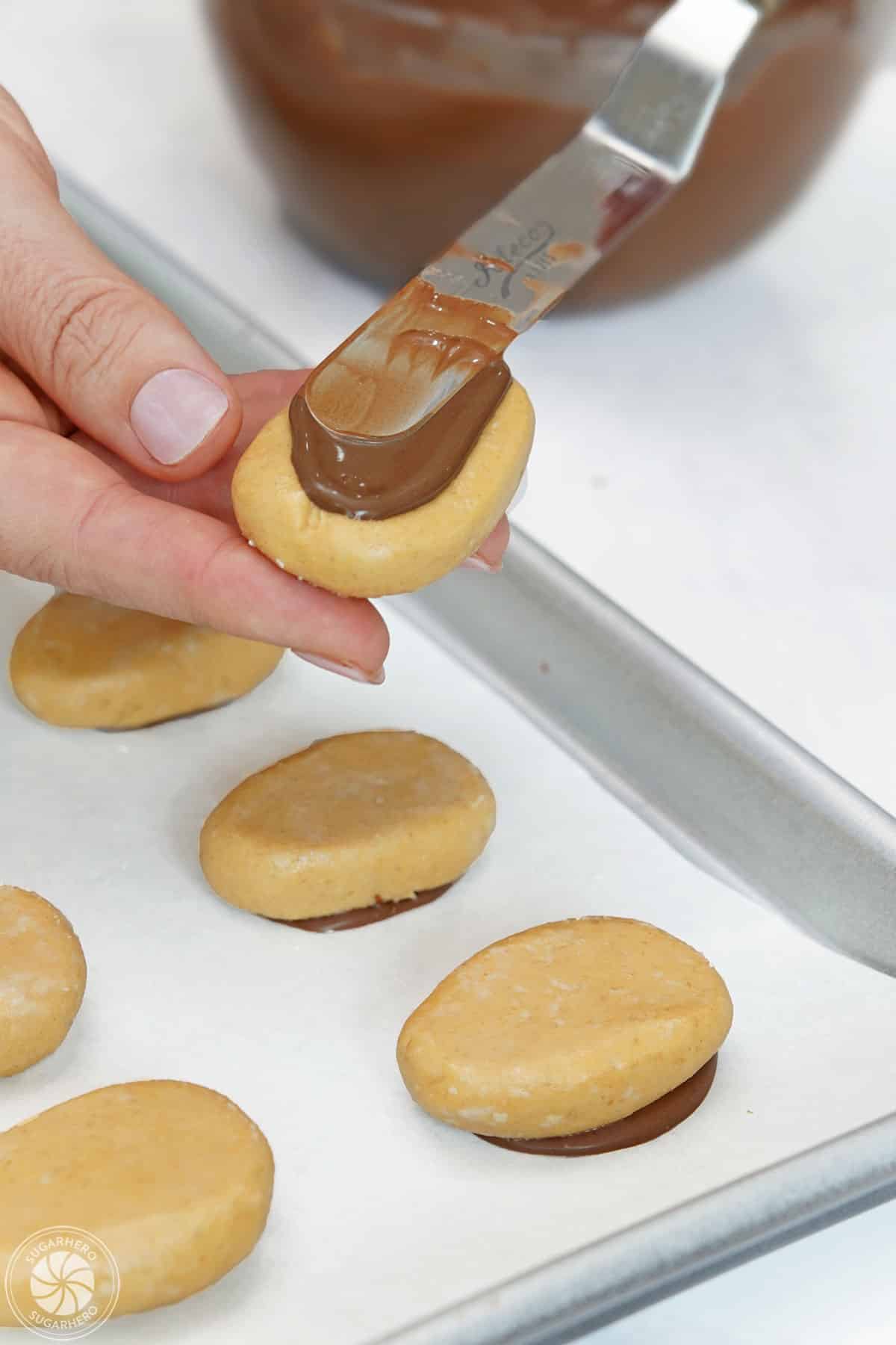 Hand spreading chocolate onto the bottom of an egg-shaped peanut butter filling.