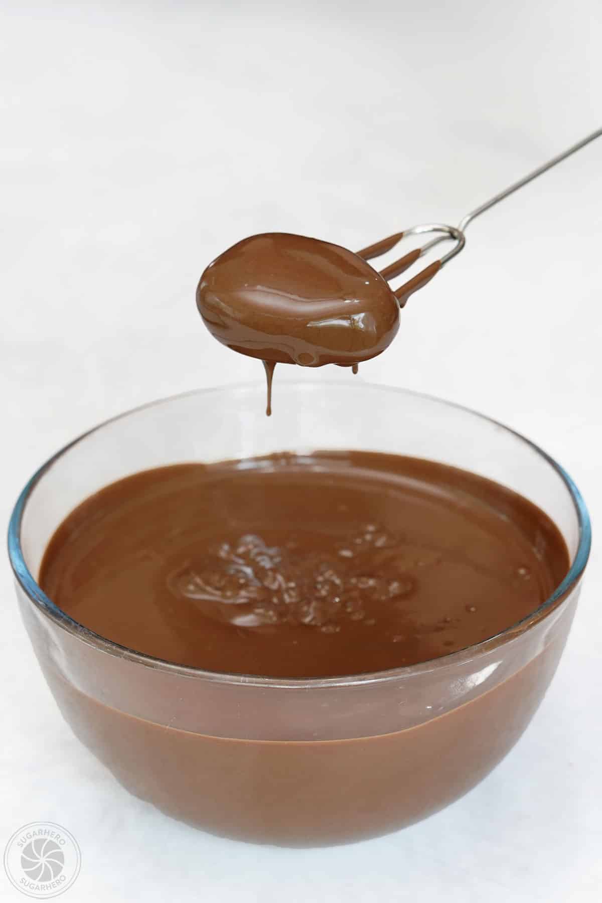 A dipping fork lifting a chocolate covered peanut butter egg out of warm chocolate.
