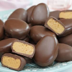 A pile of peanut butter eggs on a teal plate with a few eggs cut in half to show the center.