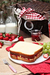 Peanut Butter and Jelly Sandwich Cake on a white plate with fruit, jam and milk in the background.