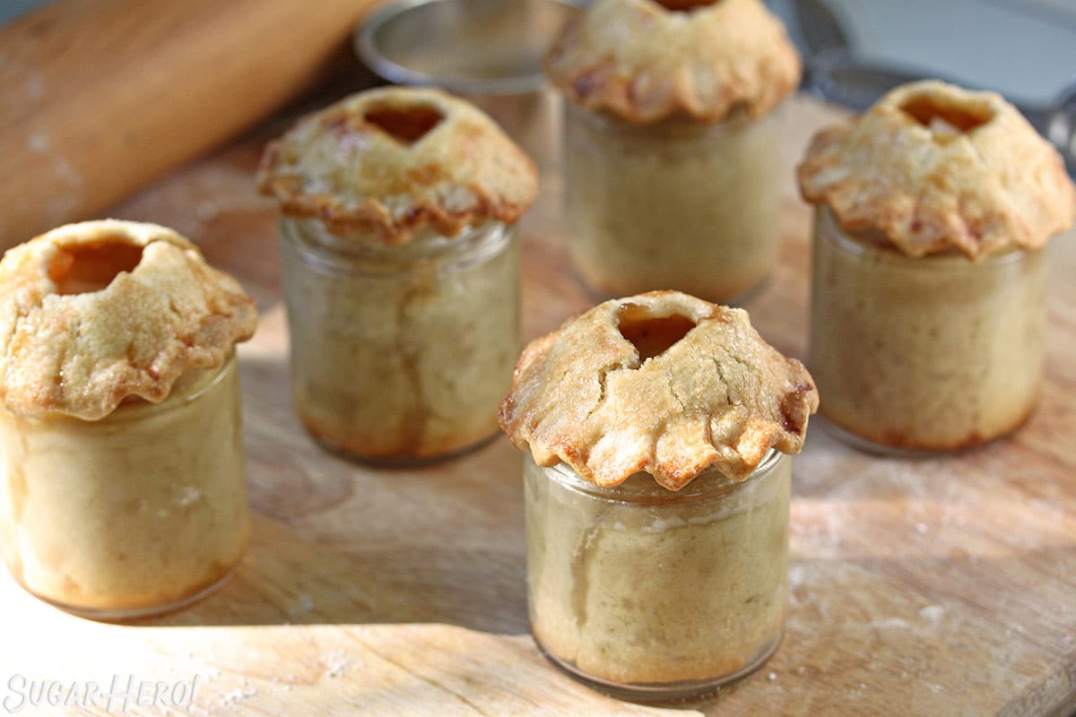 Baked pear pies in mini glass jars on a wooden cutting board.