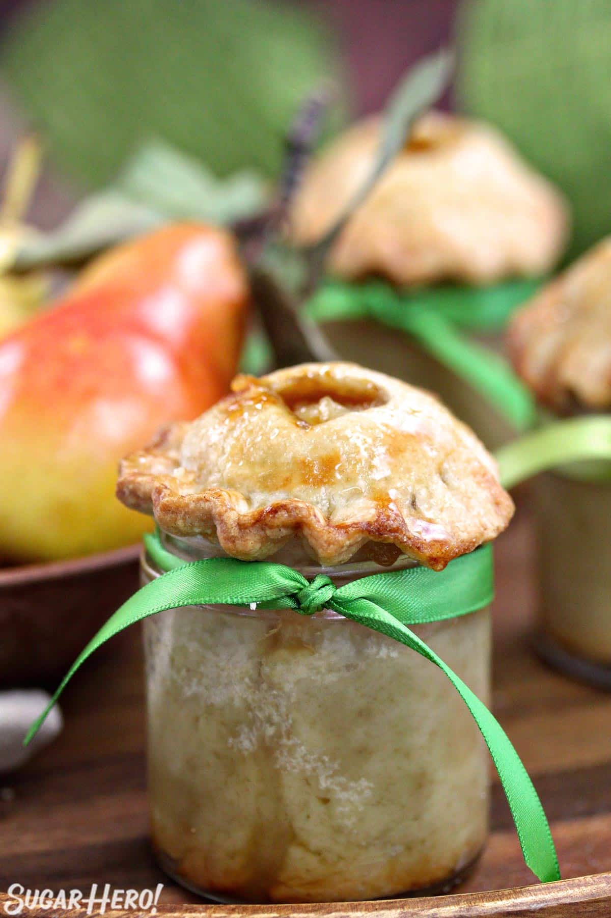 Close-up of pear pie baked in a small glass jar, with fresh pears in the background.
