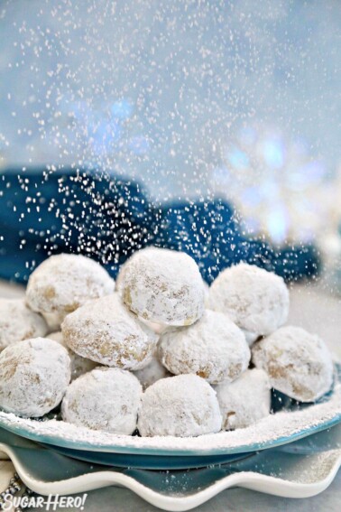 Plate of Pecan Snowball Cookies with powdered sugar being sprinkled on it.