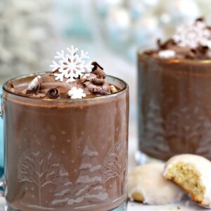 Two mugs of Peppermint Hot Chocolate topped with cocoa whipped cream and edible snowflakes.