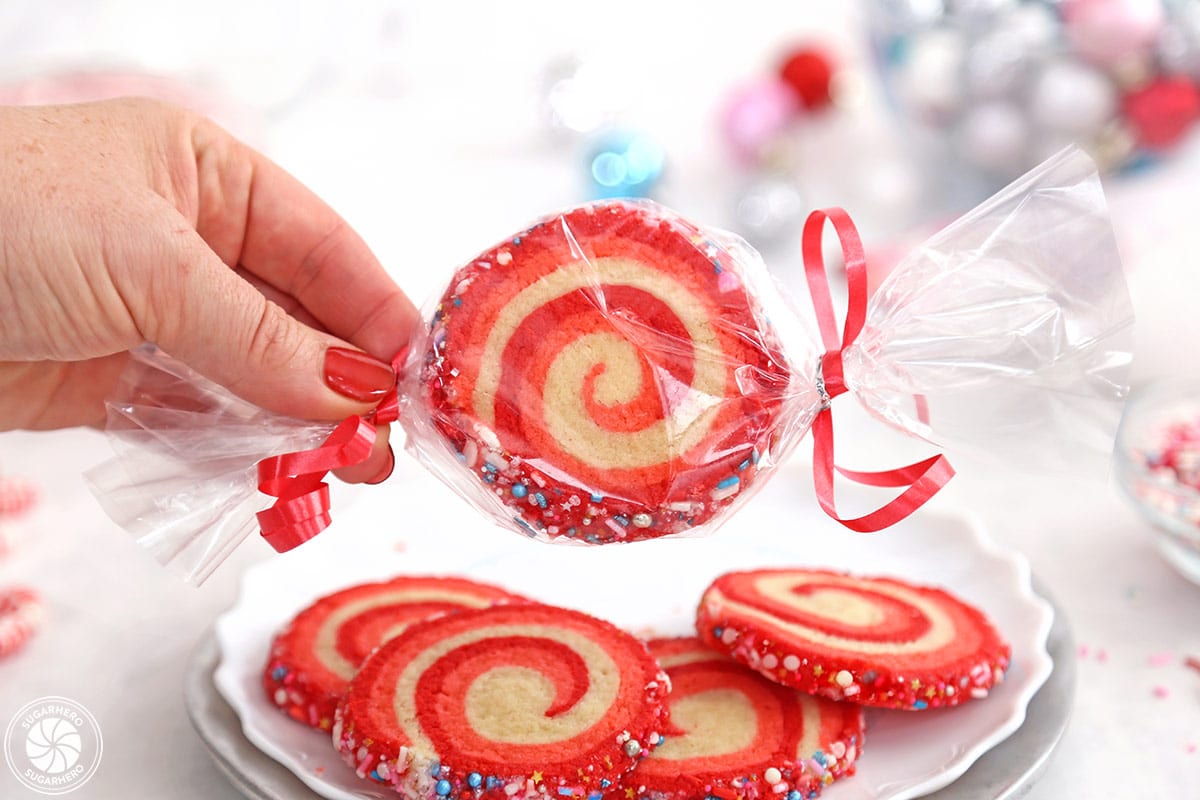 Hand holding a Peppermint Pinwheel Cookie wrapped in cellophane.