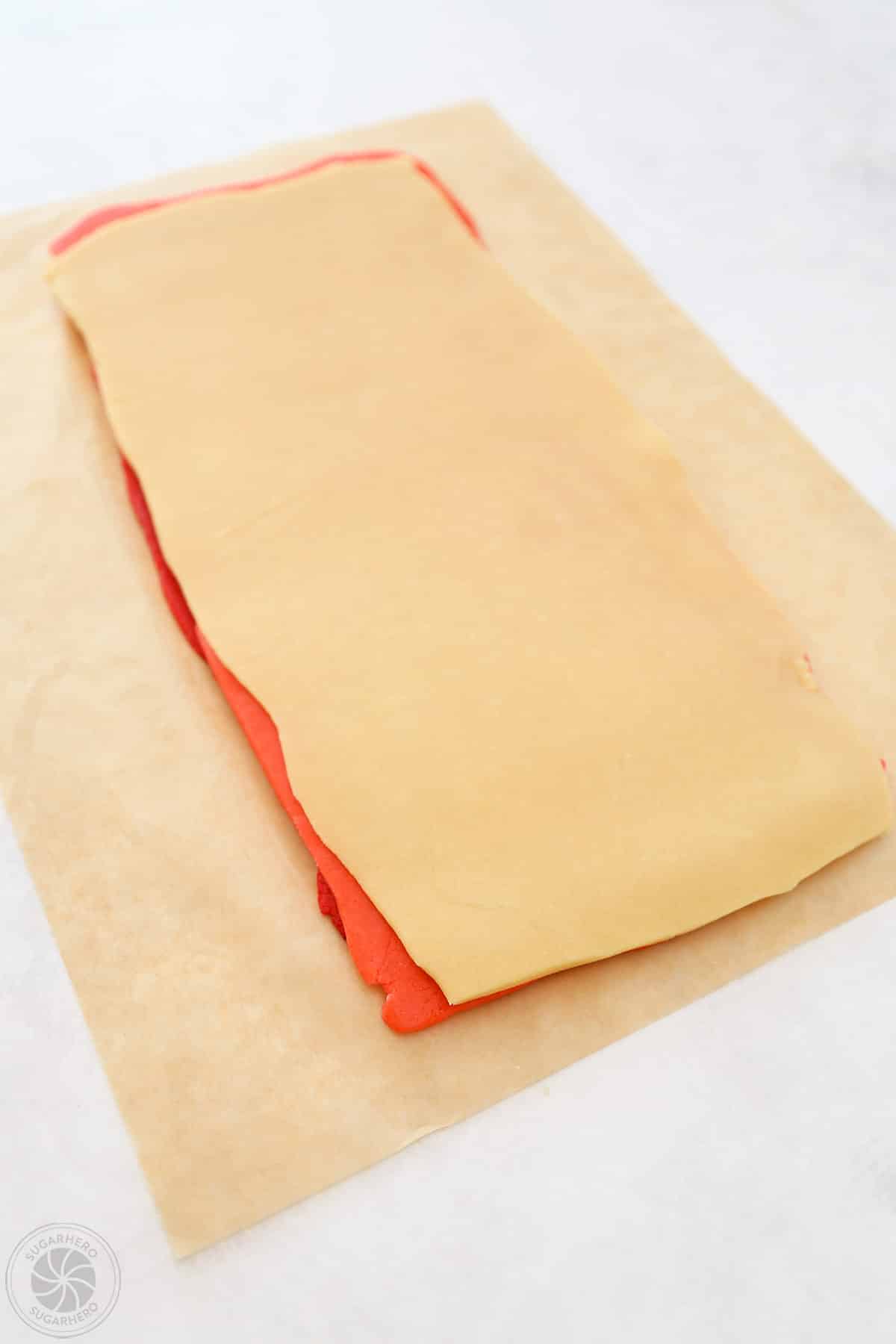 Three sheets of different colors of cookie dough stacked on top of each other, on parchment.