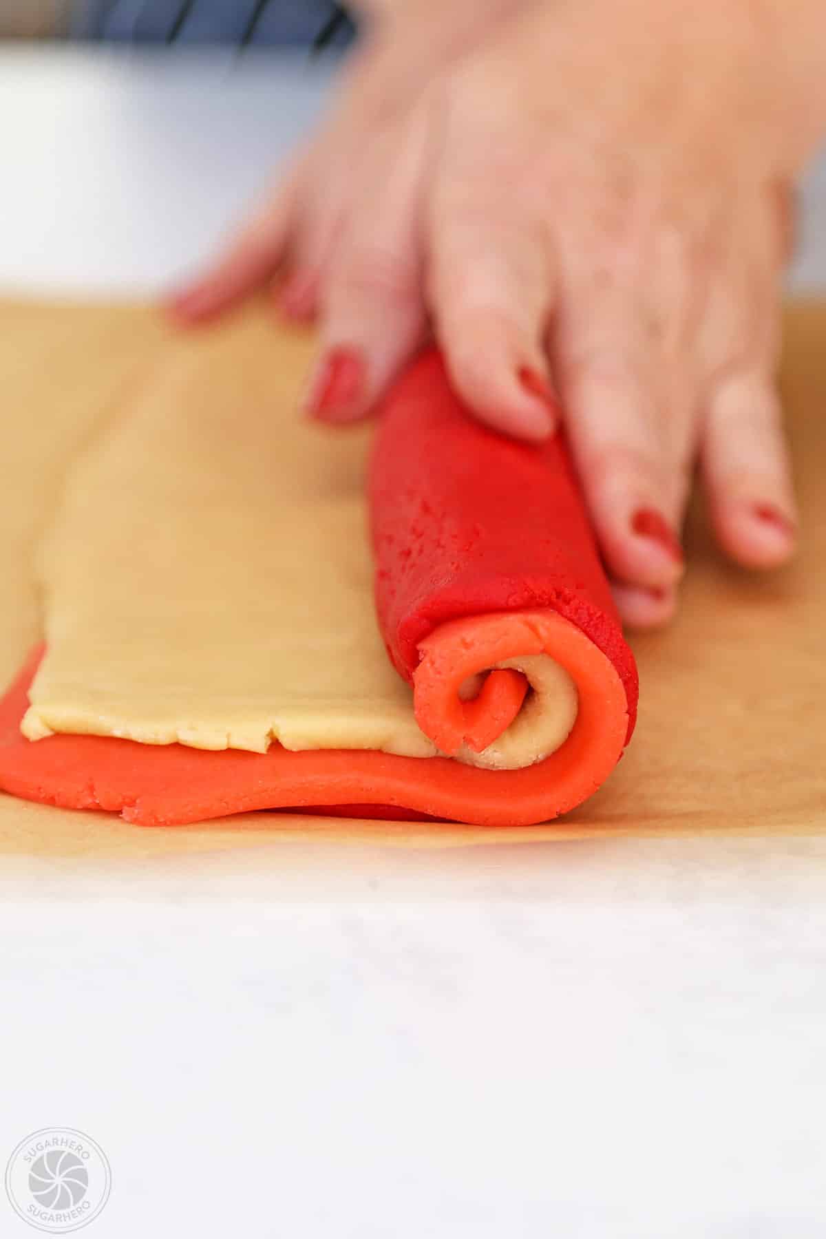 Hands rolling up tri-colored Peppermint Pinwheel Cookies.