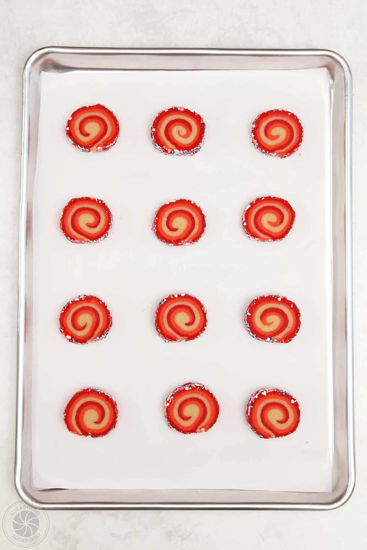 A dozen peppermint pinwheel cookies on a baking sheet.
