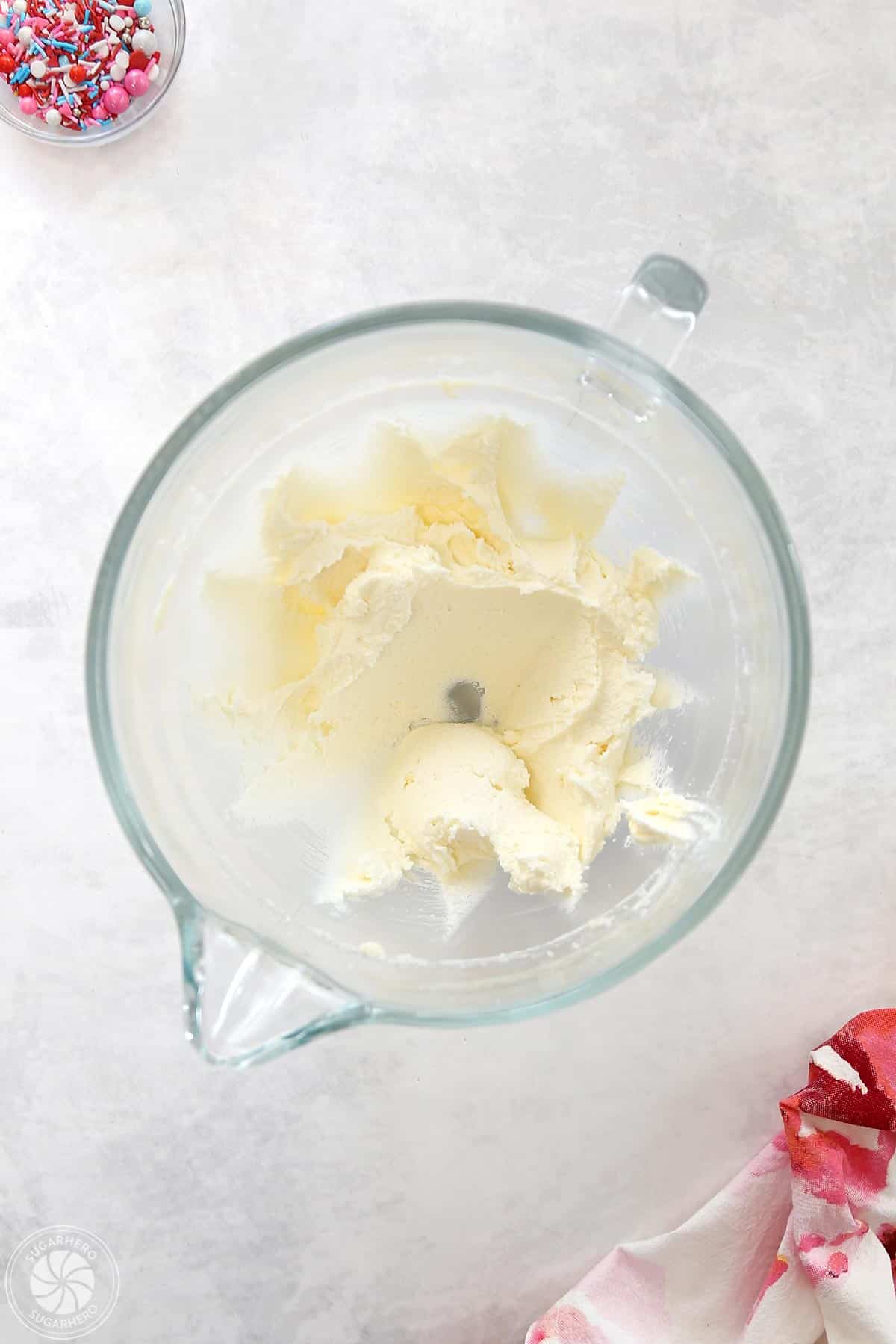 Clear glass mixing bowl with creamed butter and sugar inside.