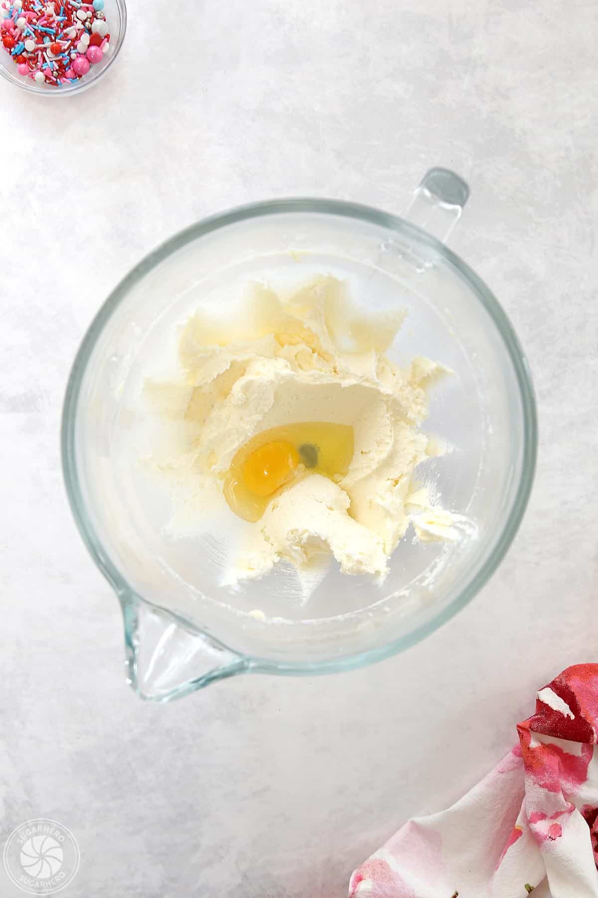 Clear glass mixing bowl with creamed butter and sugar, and an egg inside.