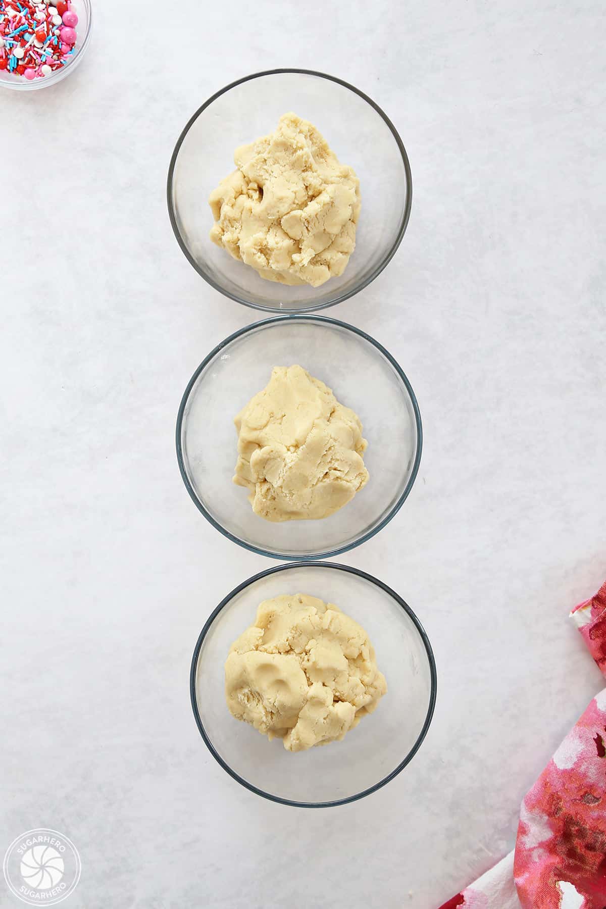 Three portions of cookie dough divided into clear glass bowls.