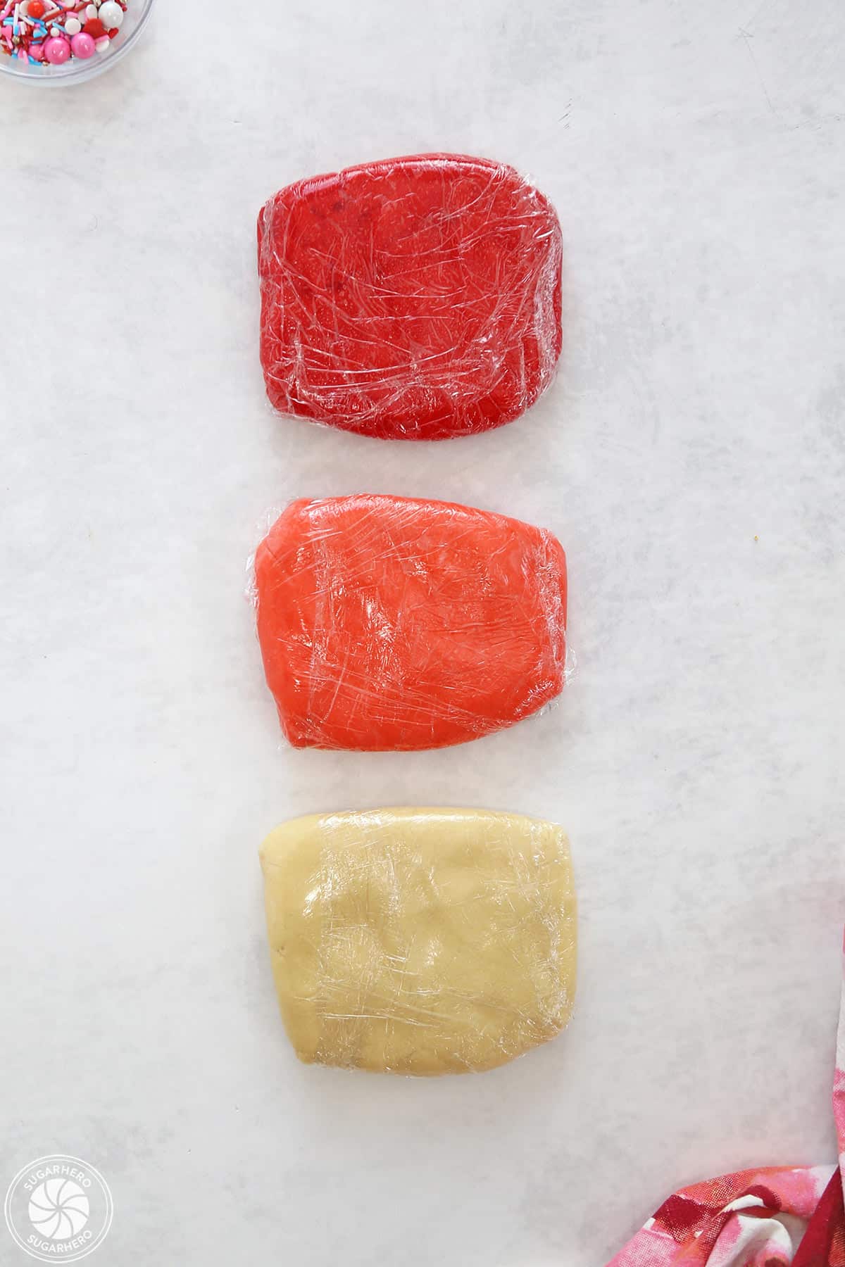 Three colors of cookie dough (red, pink, and plain) wrapped in plastic wrap.