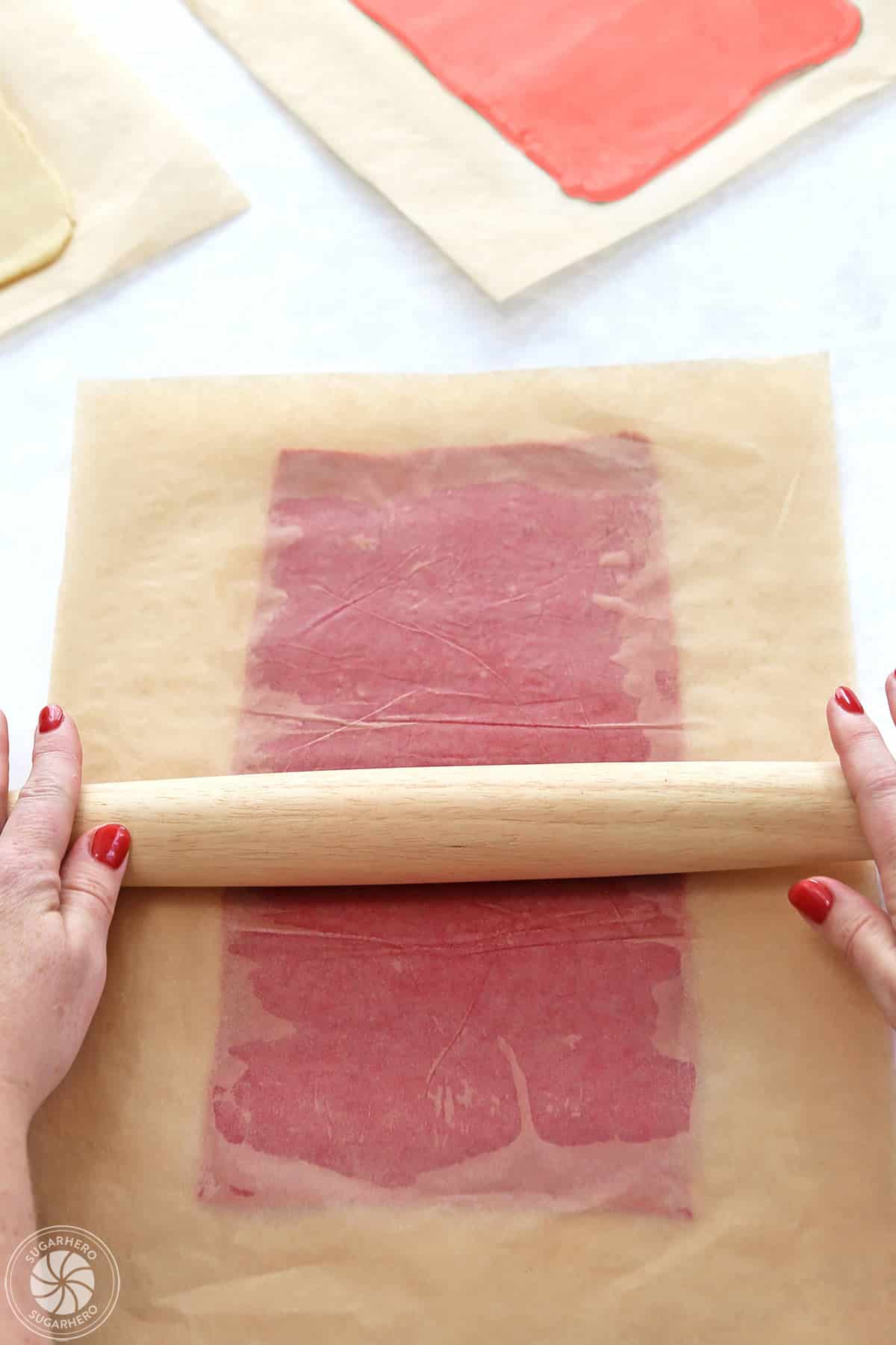 Hands rolling out red cookie dough in between sheets of parchment.