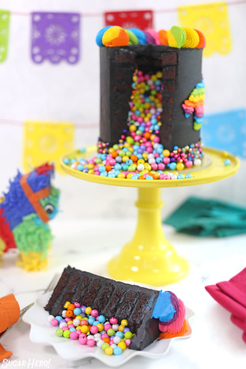 Chocolate pinata cake with candy inside on a yellow cake stand with a single piece in front