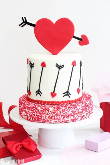 A Red Velvet Valentine's Day Cake on a white cake platter next to presents.