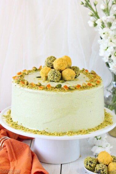 Pistachio Orange Cake on a white cake plate next to an orange napkin.