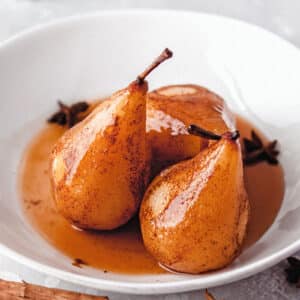 3 Poached Pears in a white bowl with their juices.