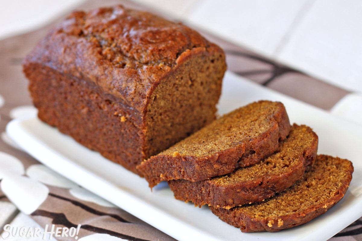 Loaf of pumpkin bread on white plate with several slices in front