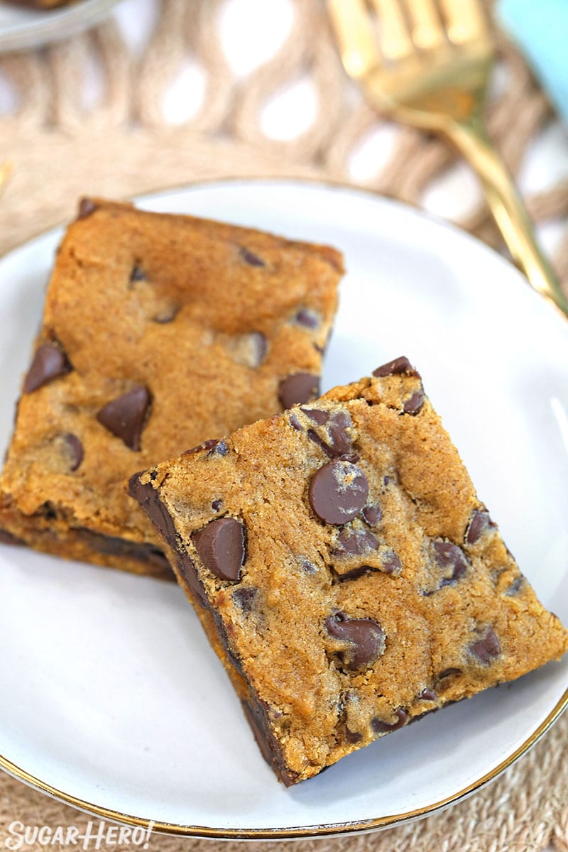 Two Pumpkin Chocolate Chip Bars on a white plate with a gold fork behind them.