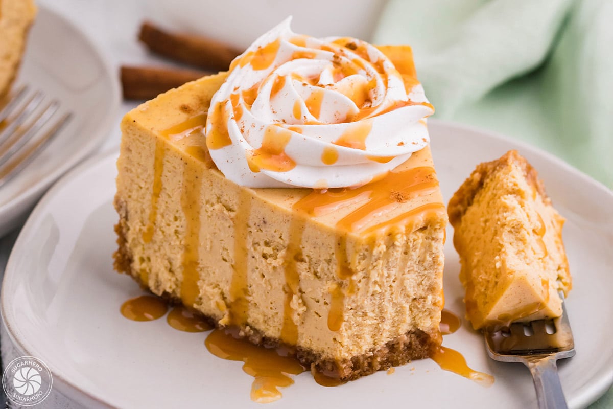 Slice of pumpkin spice cheesecake topped with whipped cream and caramel sauce.