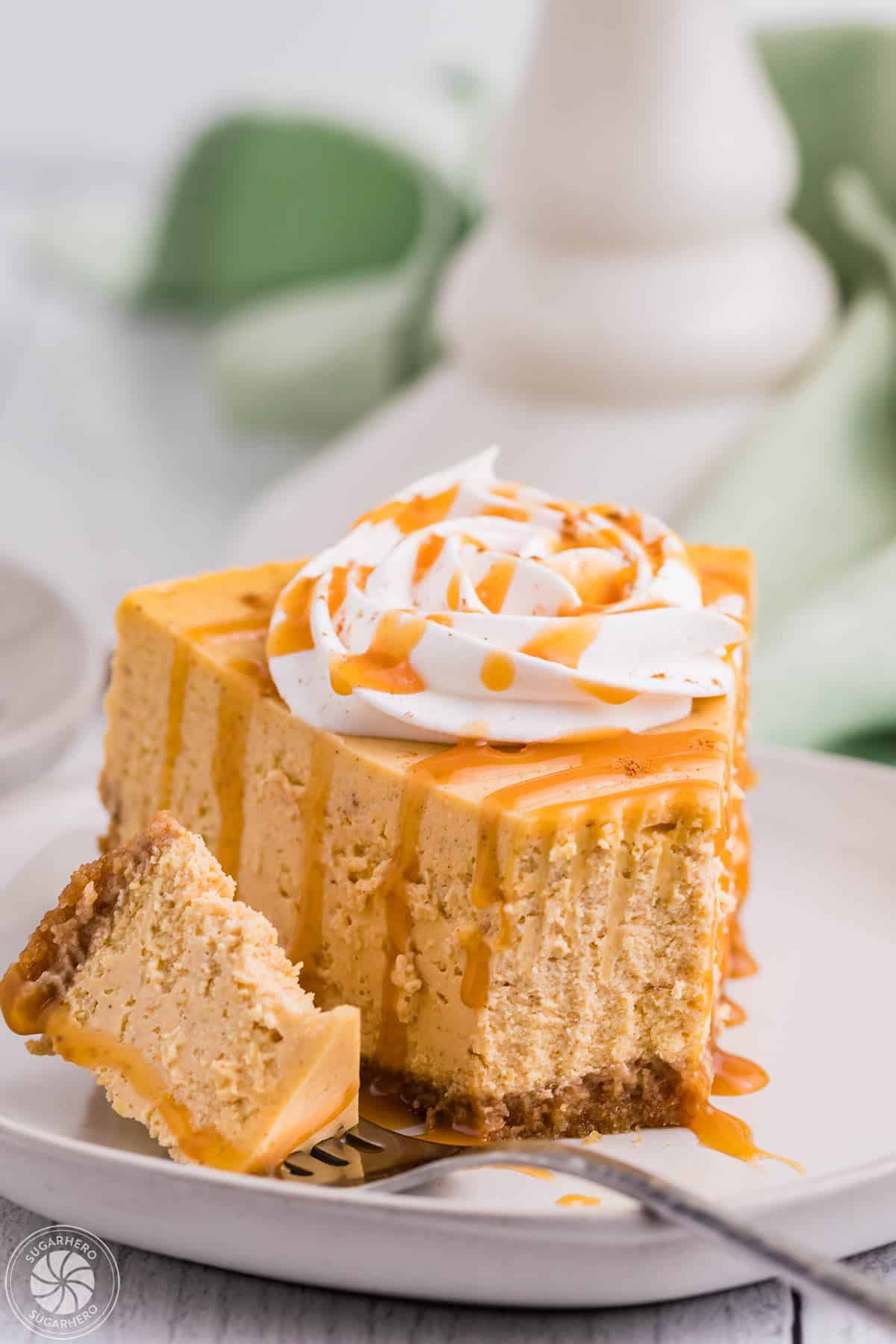 Slice of pumpkin spice cheesecake with a bite taken and set next to it on a fork on a round white plate.