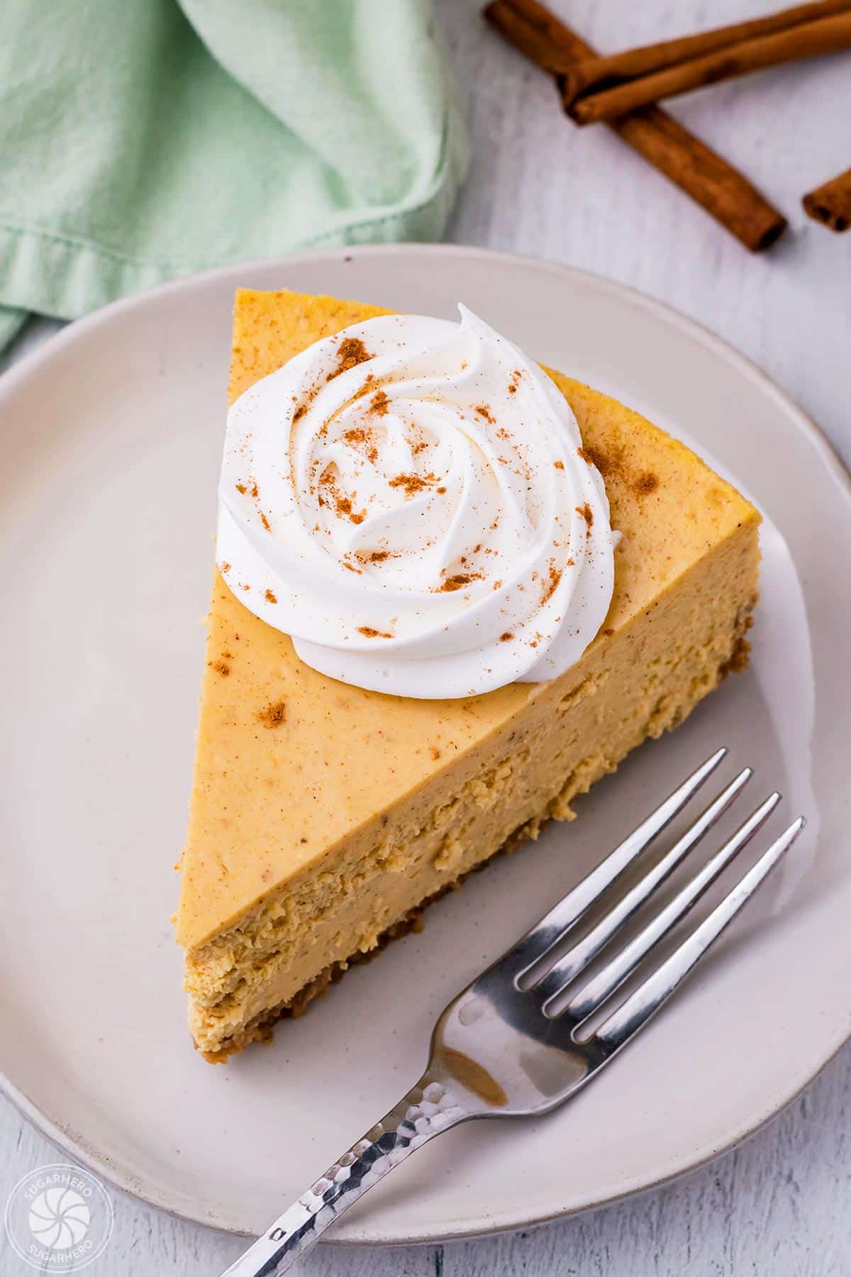 Slice of pumpkin spice cheesecake topped with a rosette of whipped cream and cinnamon.