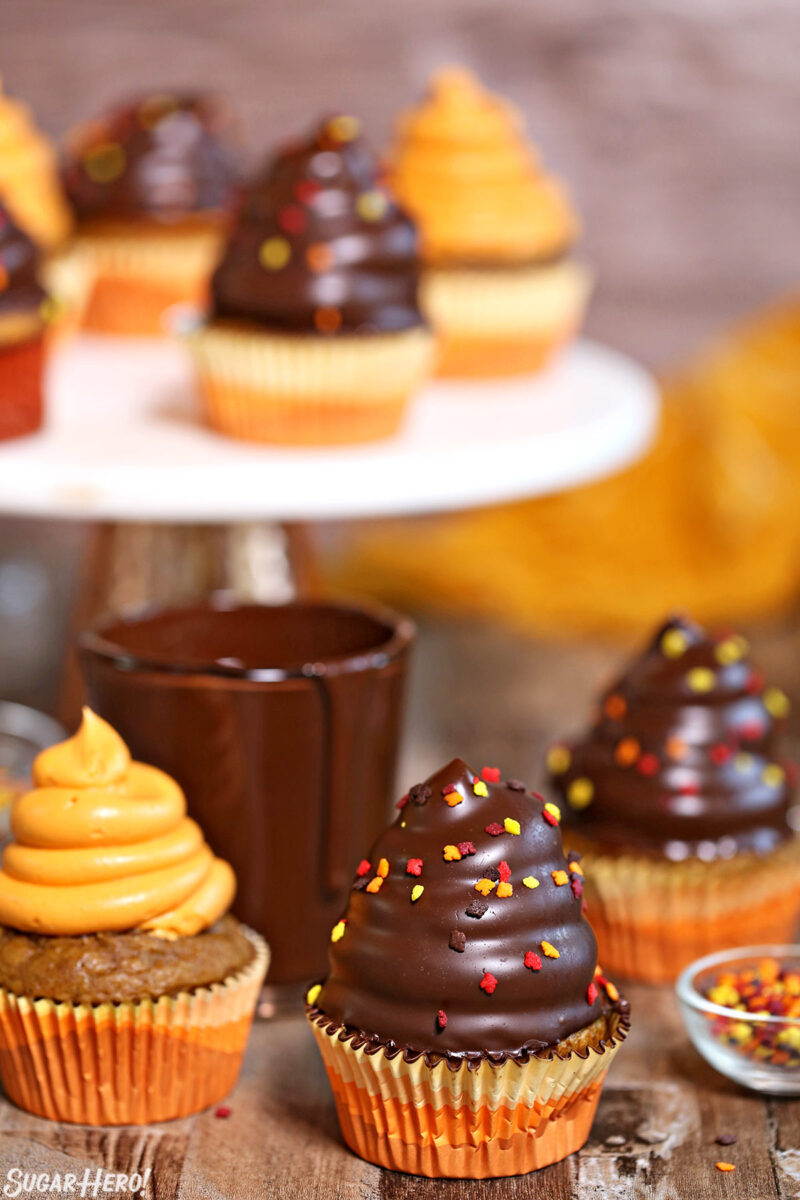 Pumpkin Spice Hi-Hat Cupcakes on a wooden surface with more cupcakes on a raised cake stand in the background.