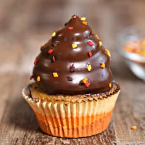 Picture of a Pumpkin Spice Hi-Hat Cupcake on a white surface with more cupcakes in the background.